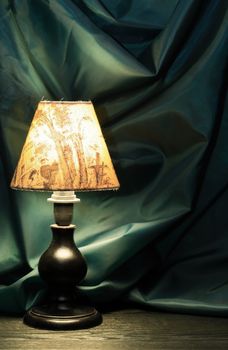 Glowing vintage table lamp with lampshade against green textile