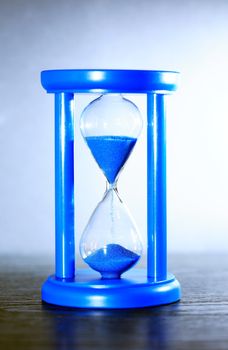 Time concept. Hourglass with blue sand on nice gray background