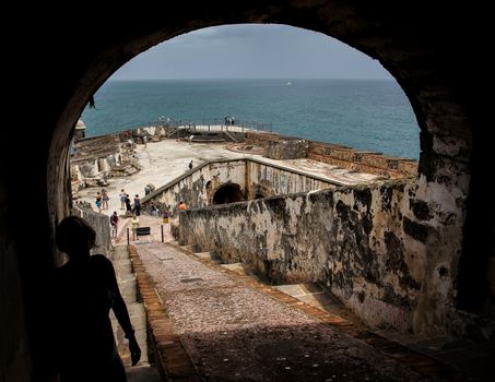 San Juan, Puerto Rico- June 15, 2013: Looking through the tunnel at Castillo San Felipe del San Moro out at the tourists exploring the fort with the Caribbean Sea in the distance.