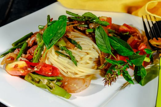 spaghetti with asparagus tomatoes bacon and herbs on wood table and white plate