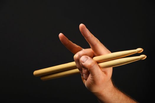 Man hand holding two drumsticks with devil horns rock metal gesture sign over black background, side view