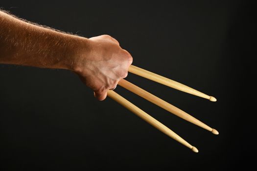 Famous wolverine claws heroic gesture, man hand holding three wooden drumsticks over black background, back view, horizontal