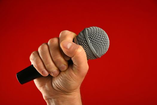 Man hand holding voice microphone in fist over red background, side view