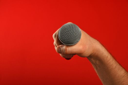 Man hand holding voice microphone in fist over red background