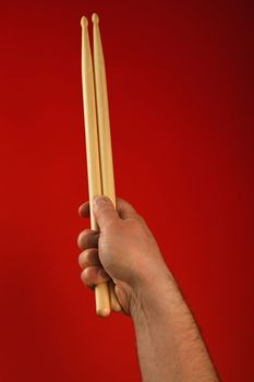 Man hand holding two wooden drumsticks over red background, point of view