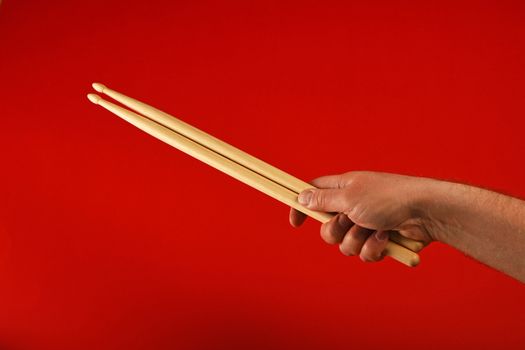 Man hand holding two wooden drumsticks over red background, diagonal