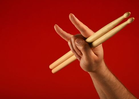 Man hand holding two drumsticks with devil horns rock metal gesture sign over red background