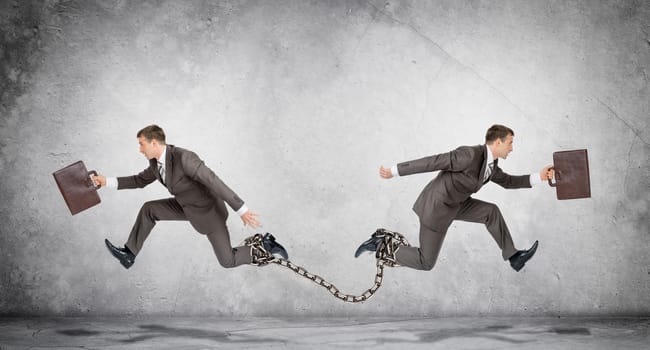 Two businessmen linked chain running in different directions on grey wall background