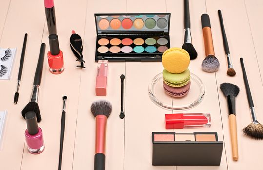 Still life, fashion woman essentials cosmetics. Beauty makeup accessories. Macarons french dessert. Lipstick, brushes, eyeshadow, false eyelashes, mascara.Unusual creative set. Vanilla wood background