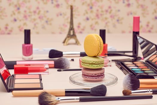 Still life, fashion woman essentials cosmetics. Beauty makeup accessories. Macarons french dessert. Lipstick, brushes, eyeshadow, false eyelashes, mascara.Unusual creative set. Vanilla wood background