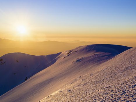 Scenic view of the sunset in the winter mountains. Direct sunlight. Sun rays. Light reflected from the snow. Clear sky. Deep shadows. Ukraine