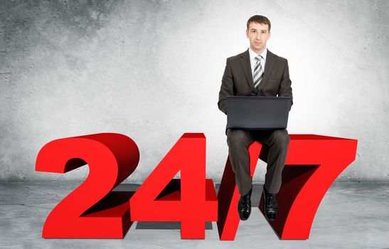 Businessman working on laptop and sitting on word 24 for 7 on grey wall background