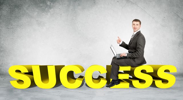 Businessman working on laptop and sitting on word success on grey wall background