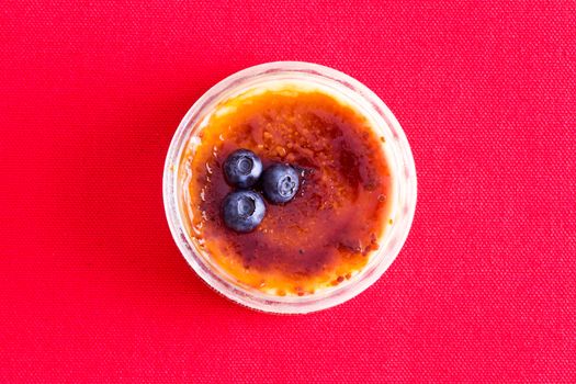 Freshly baked custard dessert topped with three blueberries from top view over red background