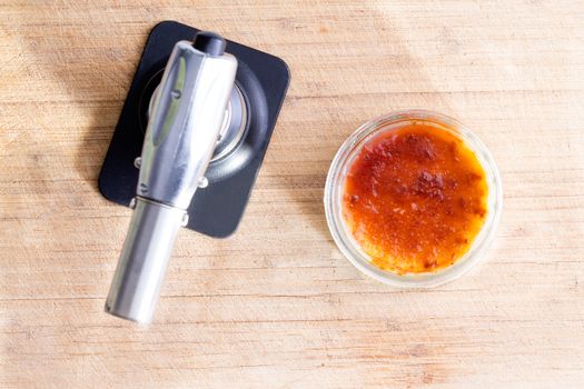 Freshly made creme brulee with a butane torch for caramelizing the suger for the traditional brittle topping, overhead view on a wooden cutting board