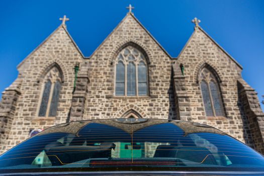 Close up of a car rear window with a Catholic church in the background. The image was taken from behind the car looking up, towards the church.