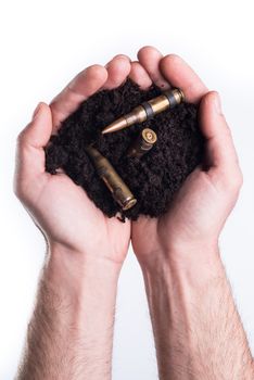 Man's hands holds topsoil with bullets on white background