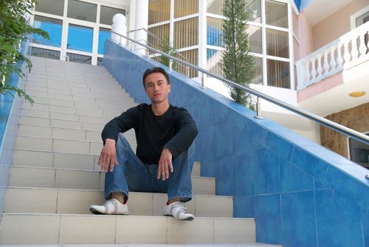 Young man sitting on the stairs of modern building