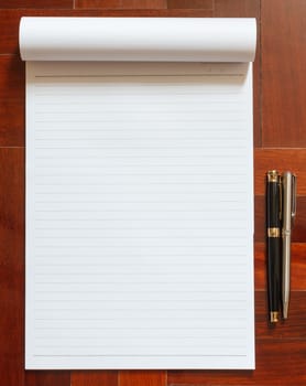 Notebook blank white page and pen. Wooden floor in the background.