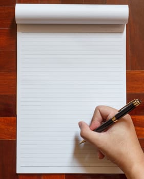 Hand write on notebook blank white page with pen. Wooden floor in the background.