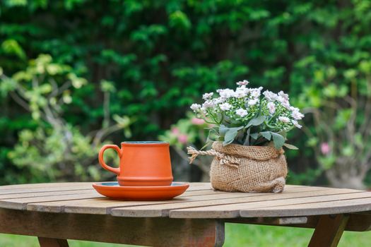 Cup of coffee and flowers on the wooden table with tree in background.Focus on the cup.