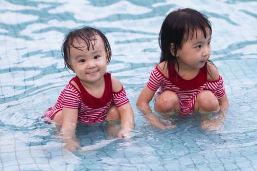 Two Little Sisters Playing in Water in Swimming Pool
