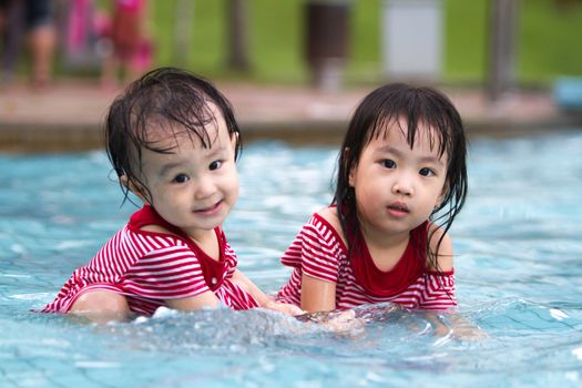 Two Little Sisters Playing in Water in Swimming Pool
