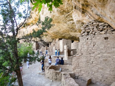 Mesa Verde, CO, USA - May 21 2008: Group of tourists visiting one of abandoned and ruined houses in pueblo located in canyon - ancient Spruce Tree House, Mesa Verde's third largest and best preserved cliff dwelling.
