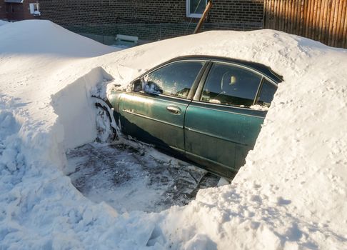 Car parked on the street covered with snow after snowfall in winter, partially cleared to enable access.
