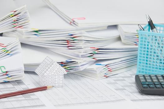 Brown pencil and house on finance account have calculator with blue pen box and step pile of document as background.