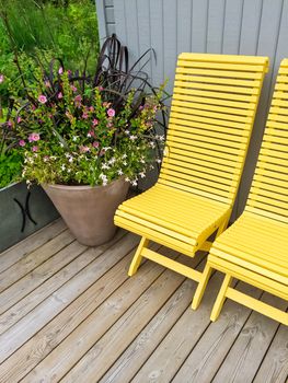 House exterior decorated with yellow chairs and big pot with flowers.