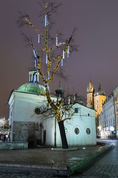 The Church of St. Adalbert on Rynek, in Krakow, one of the oldest churches in Poland. Decorated tree in the foreground, St. Mary's basilica in the background.