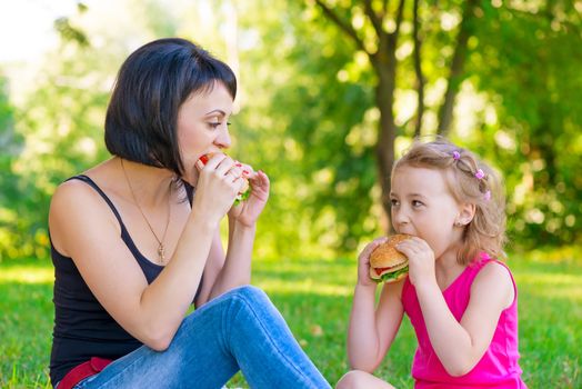 Mother and daughter eating sandwiches at a picnic in the park