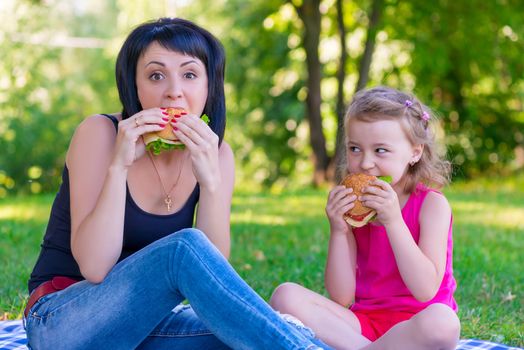 Mom and daughter eating tasty burgers on a picnic