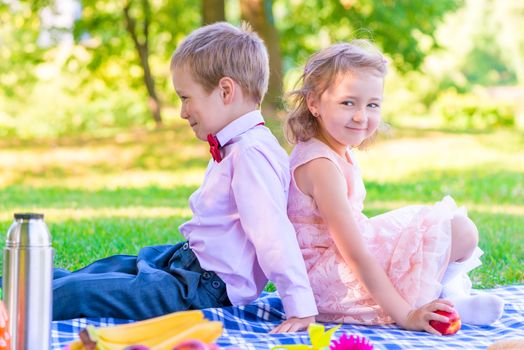 boy and a girl of 6 years on a picnic sitting back to back