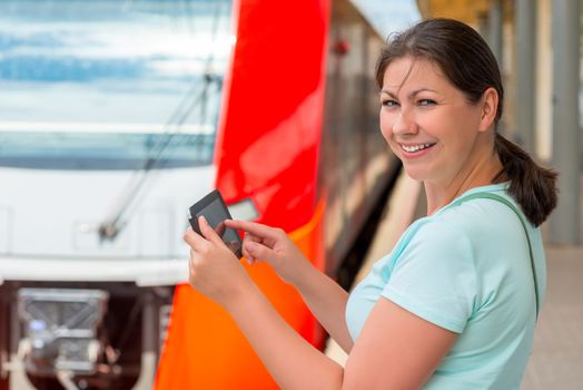 cheerful girl with tablet computer is at the station waiting the train boarding