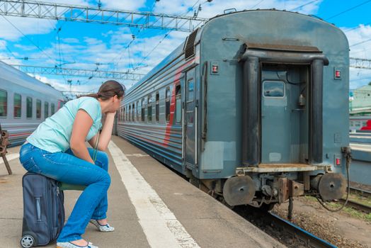 woman sitting on a suitcase and looking at the departing train