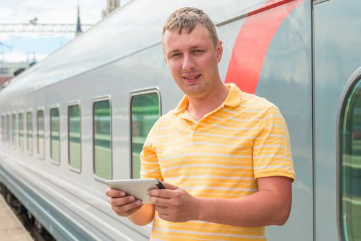 Happy man holding a tablet computer near the train