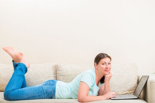 girl in jeans and a T-shirt on the couch with a laptop