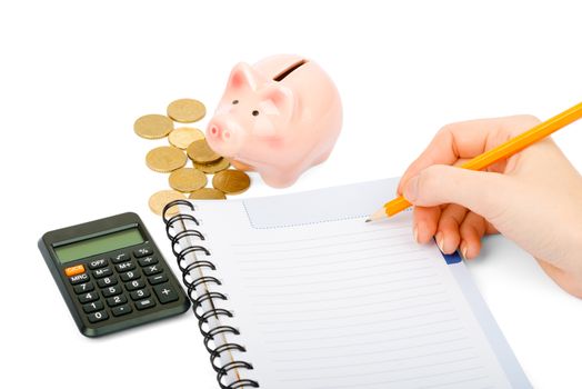 Writing notes or planning schedule on blank spiral notebook with calculator and piggy bank