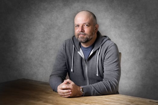 Portrait of a friendly looking, balding and unshaven man sitting on a wooden table