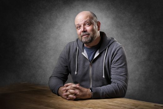 Portrait of a friendly looking, balding and unshaven man sitting on a wooden table