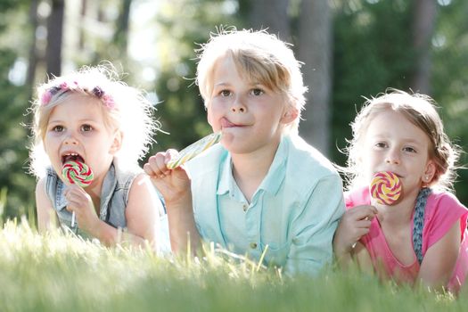 Group of happy children eating lollipops outdoors in summer park