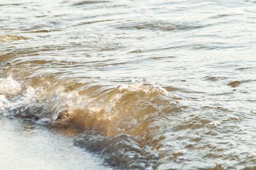 surf on a sandy beach with waves at sunset