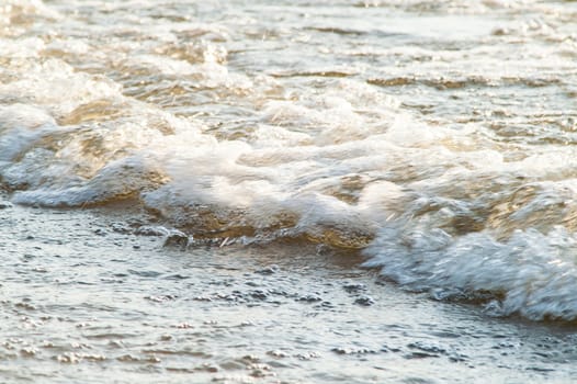 surf on a sandy beach with waves at sunset