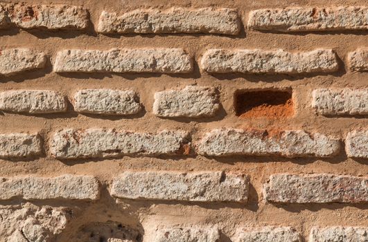 Wall made of bricks, enlightened by the sunlight. Some bricks missing.