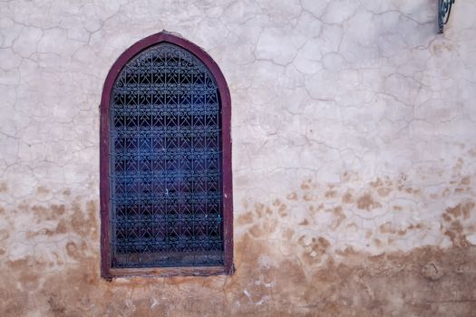 Old wall with a window with ornamental grating. Contrast frame around the window.