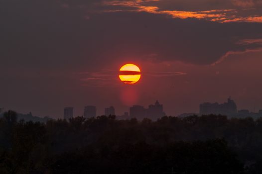 the sun at sunset with clouds over the city and trees
