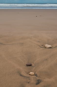 Several stones in the wet sand after a tide. Golden color of the sand. Line of the Atlantic ocean in the background.