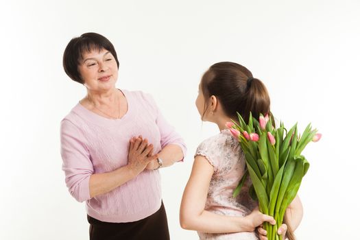 the granddaughter hides a bouquet of flowers for the grandmother behind the back